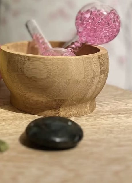 Un bol de bambou, deux boules de verre rose et un galet noir sur une table en bois